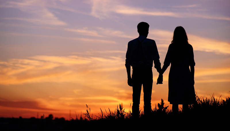 couple holding hands silhouetted against the sunset
