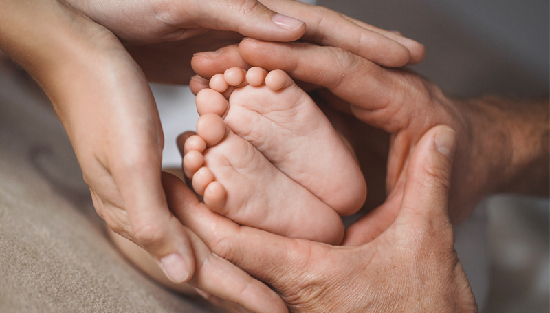 adoptive parents cradling newborn baby's feet in their hands