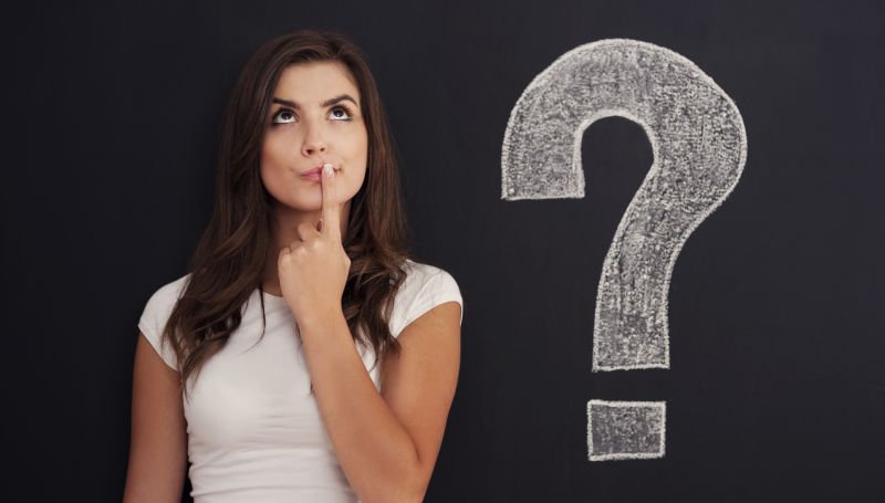 inquisitive young woman stands nexts to chalkboard with question mark