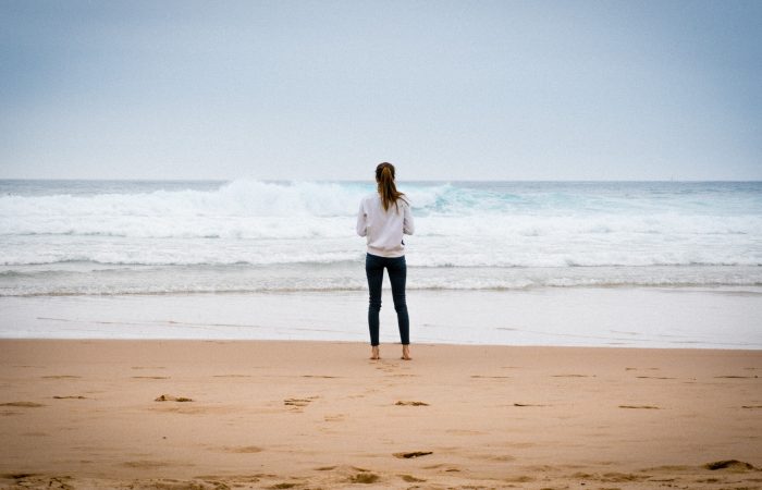 a young woman standing on a beach looking out at the ocean